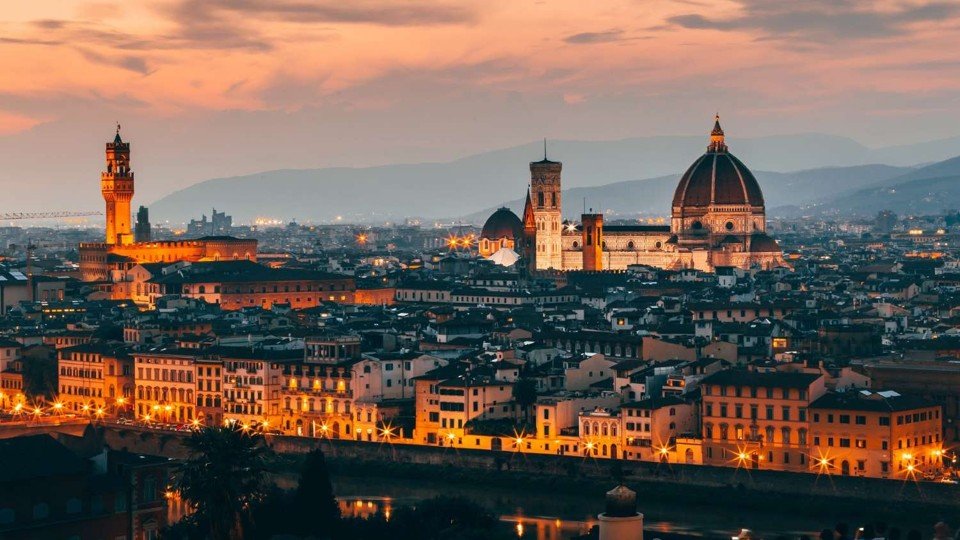 Florence skyline at sunset with the Duomo cathedral dome silhouetted against an orange and purple sky