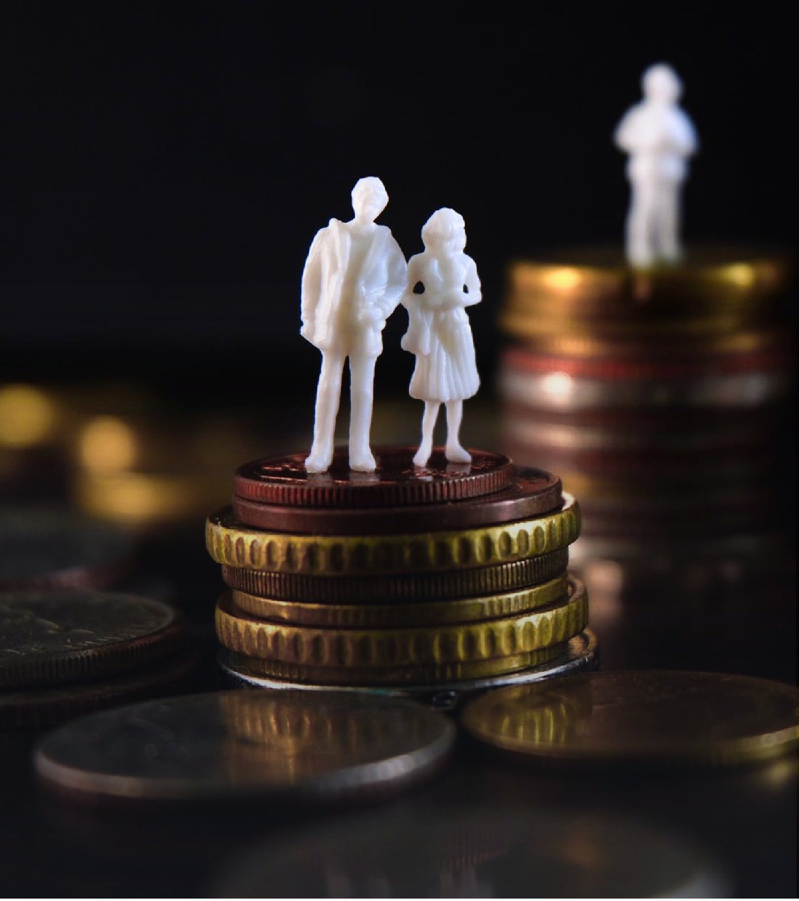 Miniature figurines of a family standing on stacked coins symbolizing savings