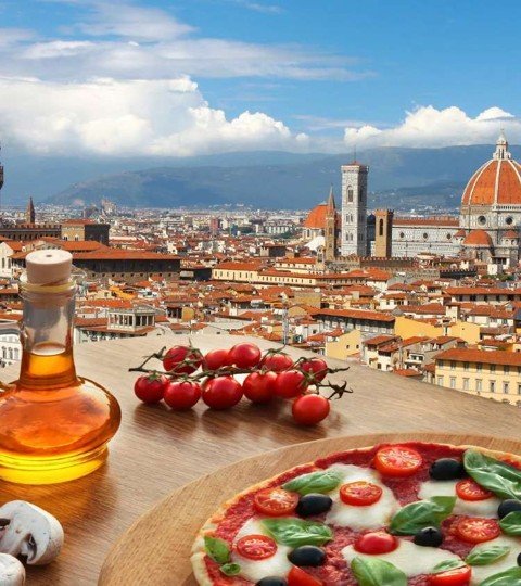 View of Florence rooftops and the Duomo with a table of fresh tomatoes, olive oil, and pizza in the foreground