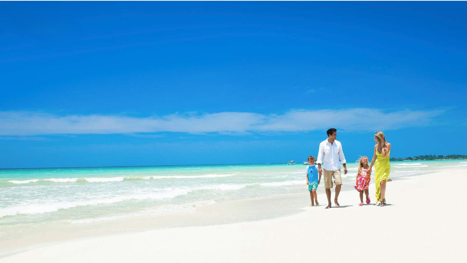 Family of a father, mother, and two children walking together on a tropical white sand beach