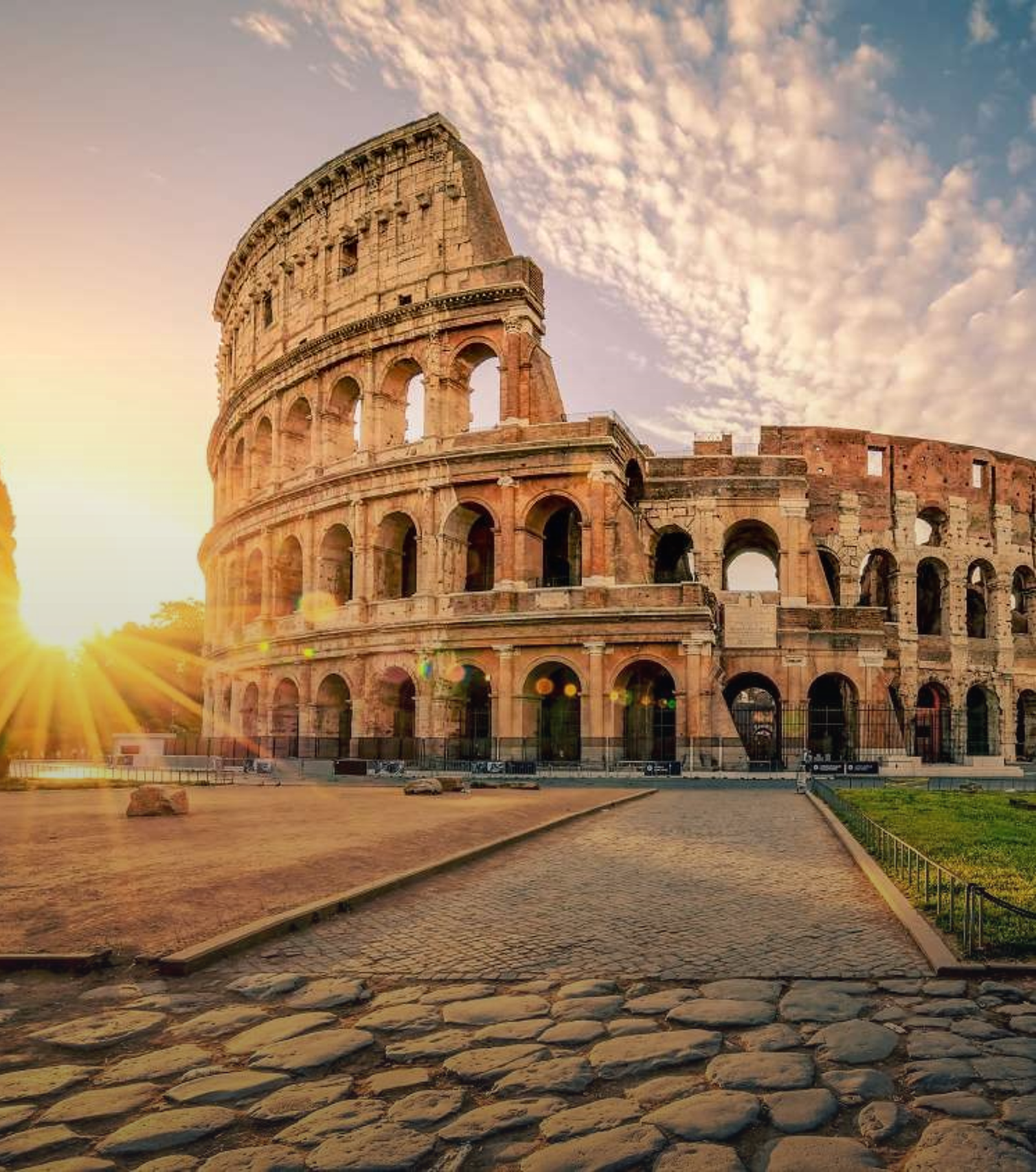 The Colosseum in Rome bathed in golden sunrise light with sun rays over a cobblestone road